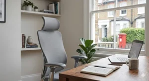 A professional woman working comfortably in a grey mesh designer desk chair within a bright British home study.