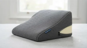 Close-up of a contoured orthopaedic memory foam wedge cushion showing its ergonomic slope, grey fabric cover, and visible foam core.