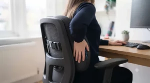 Person pointing to their lower back while sitting comfortably against an ergonomic support cushion.